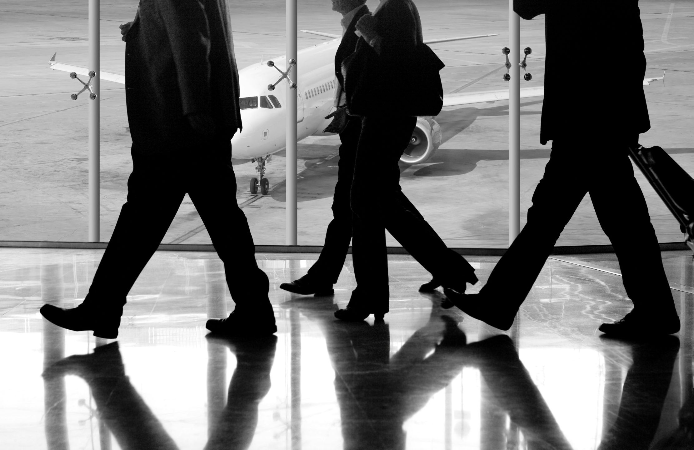 Black and white picture, showing an airplane and people walking in a airport.